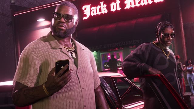 Boobie and Dre'Quan exiting a car. Boobie holds his phone while Dre'Quan leans against the open car door.