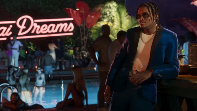 Dre'Quan leaning against a bar wearing a suit at a nighttime pool party. Guests in the background are wearing swimsuits.