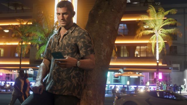 Jason outside on the street leaning against a tree while looking at his phone.