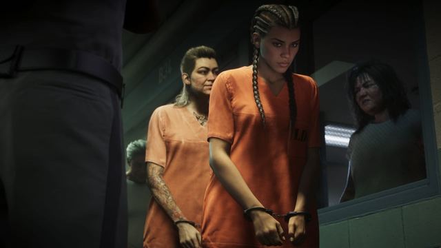 Inside a jail, Lucia and another woman are handcuffed and wearing orange jumpsuits as they walk by a window where another woman watches through the glass. An officer stands nearby.