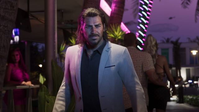 Raul wearing a suit looks off into the distance. In the background people walk down a neon-lit sidewalk.